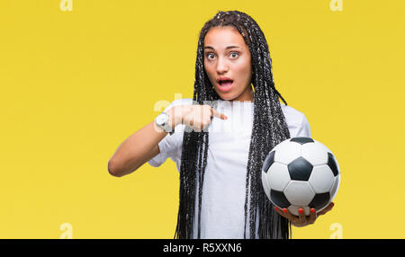 Giovani capelli intrecciati African American Girl tenendo palla calcio su sfondo isolato con sorpresa faccia puntare il dito a se stesso Foto Stock