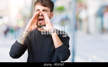 Giovane uomo bello su isolati che urlava arrabbiato ad alto volume con Mani sulla bocca Foto Stock