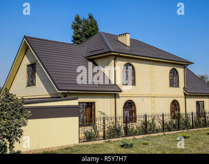 Casa del mattone giallo e marrone e tetto ondulato in metallo. Tralicci su windows. Foto Stock