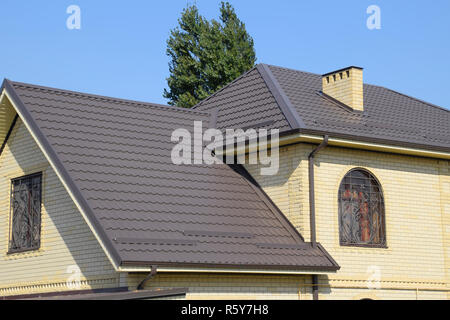 Casa del mattone giallo e marrone e tetto ondulato in metallo. Tralicci su windows. Foto Stock