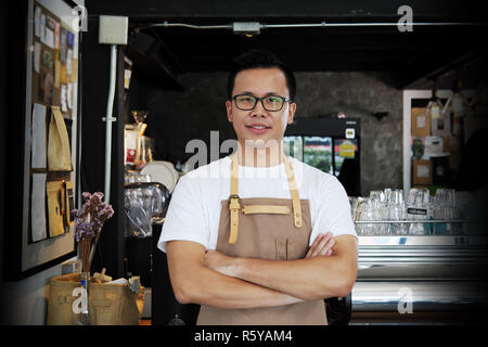 Ritratto di sorridere asian barista con le braccia incrociate al contatore nel coffee shop. Il cafe ristorante servizio, industria alimentare e delle bevande del concetto. Foto Stock