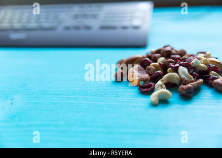 Un sano spuntino veloce in ufficio. La frutta secca e i dadi sulla scrivania con computer. Foto Stock