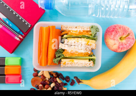 Scuola scatola di pranzo con sandwich, verdure, acqua, dadi e frutti su sfondo turchese. Abitudini alimentari sane concept Foto Stock