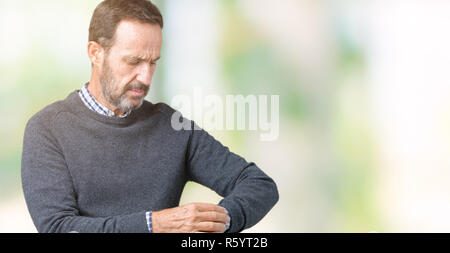 Bella la mezza età senior uomo che indossa un maglione sopra isolato background controllando il tempo su orologio da polso, rilassato e fiducioso Foto Stock