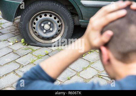 Preoccupato Un uomo guarda forato pneumatici per auto Foto Stock