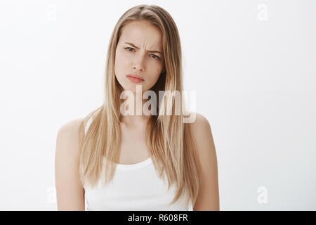 Ragazza sospetta qualcosa di sbagliato essendo dubbia in amico dire tutta la verità, strizzare gli occhi sospettosi in telecamera come accigliata e rendendo faccia esitante, stand Foto Stock