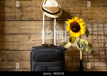 Concetto di viaggio. Valigia, hipster hat, girasole e occhiali da sole sulla parete in legno sfondo. Foto Stock