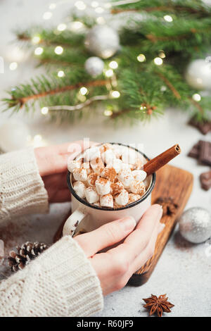 Azienda tazza di cioccolata calda con marshmallows e cannella. Ragazza in maglia maglione holding bevanda calda. Messa a fuoco selettiva. Accogliente il concetto di Natale Foto Stock