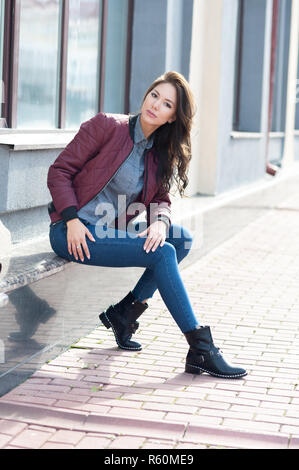 Giovane bella donna elegante in un pilota di borgogna giacca e jeans blu, street style, Primavera e autunno trend, guardare, capelli al vento Foto Stock