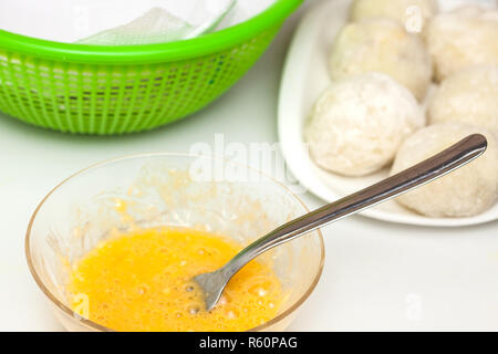 Fasi di preparazione del tradizionale piatto colombiano chiamato patate ripiene: Dunking patate ripiene di uovo e farina Foto Stock