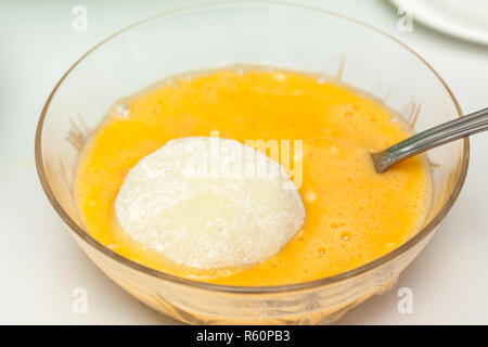 Fasi di preparazione del tradizionale piatto colombiano chiamato patate ripiene: Dunking patate ripiene di uovo e farina Foto Stock