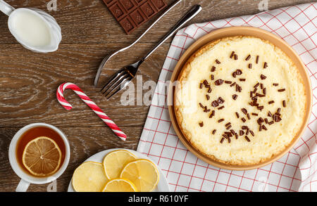 In casa la cheesecake cosparso con scaglie di cioccolato, tè con limone e Natale candy su uno sfondo di legno. Vista superiore Foto Stock