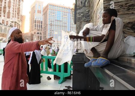 La Mecca, Arabia Saudita - 02 Marzo 2017: un piccolo bambino aiuta a dare un sacchetto di plastica come un contenitore di sandali di adoratori Foto Stock