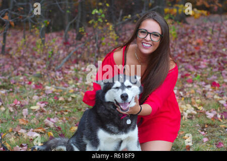 Giovane donna abito rosso a giocare con un cane in un parco Foto Stock