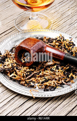 Bicchiere di cognac e il tubo con il tabacco sul vecchio tavolo in legno Foto Stock