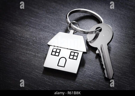 Le chiavi di casa su una casa portachiavi sagomato in appoggio su uno sfondo di legno concept per il settore immobiliare, casa mobile o locazione Foto Stock