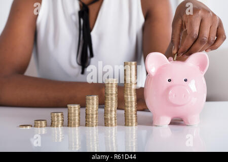 Mano umana mettendo in moneta Piggybank Foto Stock