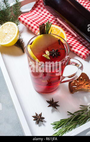 Vin brulè, una bottiglia di vino rosso, Abete rami, cannella, arancio e limone sul vassoio bianco su sfondo di calcestruzzo. Bevande d'inverno. Vigilia di Natale Foto Stock