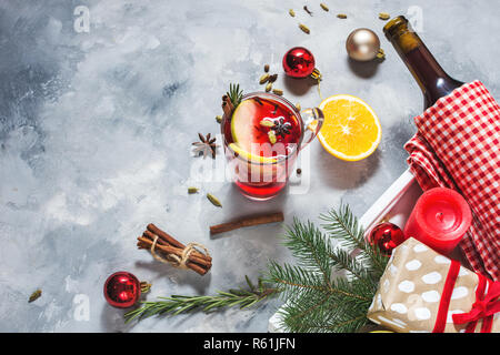 Vin brulè, una bottiglia di vino rosso, Abete rami, cannella, limone e arancio su sfondo di calcestruzzo. Bevande d'inverno. Vigilia di Natale Foto Stock