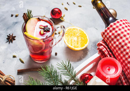 Vin brulè, una bottiglia di vino rosso, Abete rami, cannella, limone e arancio su sfondo di calcestruzzo. Bevande d'inverno. Vigilia di Natale Foto Stock