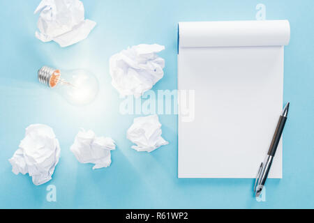 Vista in pianta del fustellato di notebook con carta sbriciolato palle e incandescente lampadina luce su sfondo blu, avere idee nuove concept Foto Stock