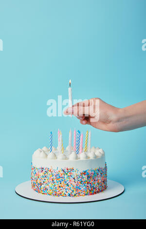 Vista parziale di donna mettendo candela di illuminazione sulla torta di compleanno su sfondo blu Foto Stock