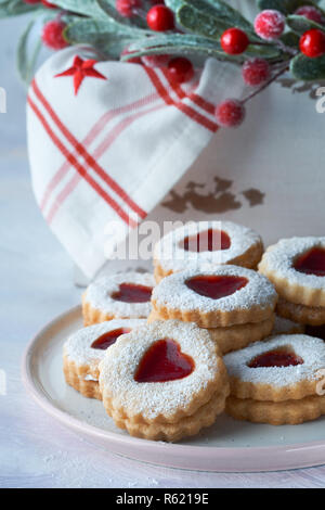 Piastra del tradizionale Natale Linzer cookie riempito con confettura di fragole sul tavolo bianco con decorazioni di Natale in verde e rosso Foto Stock