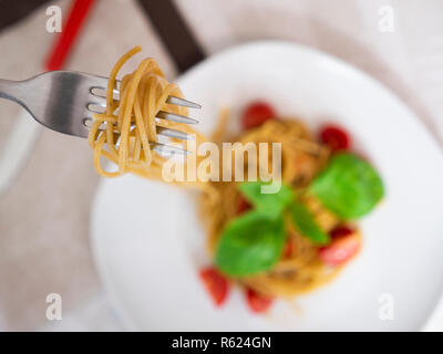 Giovane donna di mangiare spaghetti integrali con pomodori e basilico Foto Stock