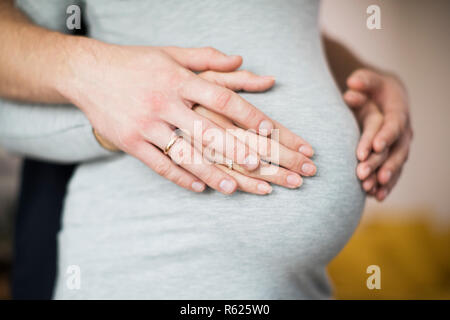 Close Up di maschio e femmina mani appoggiate sulla gravidanza Womans Stomaco Foto Stock
