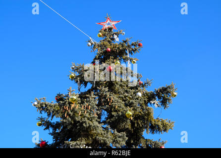 Decorazioni Anno nuovo albero. Tinsel e giocattoli, le sfere e le altre decorazioni di Natale sulla struttura ad albero di Natale in piedi in aria aperta. Foto Stock