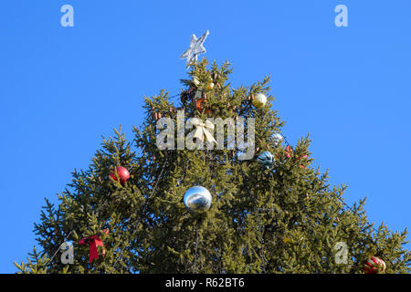 Decorazioni Anno nuovo albero. Tinsel e giocattoli, le sfere e le altre decorazioni di Natale sulla struttura ad albero di Natale in piedi in aria aperta. Foto Stock