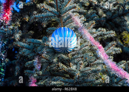 Decorazioni Anno nuovo albero. Tinsel e giocattoli, le sfere e le altre decorazioni di Natale sulla struttura ad albero di Natale in piedi in aria aperta. Foto Stock