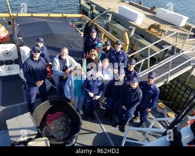 Costa guardie e membri del North Carolina Aquarium sull Isola Roanoke posano per una fotografia a bordo di Guardacoste Heron offshore Cape Henry, Virginia, nov. 18, 2018. L'equipaggio ha lavorato con il personale di acquario per rilasciare 14 riabilitato le tartarughe di mare che erano storditi a freddo a causa della diminuzione delle temperature dell'acqua. Foto Stock