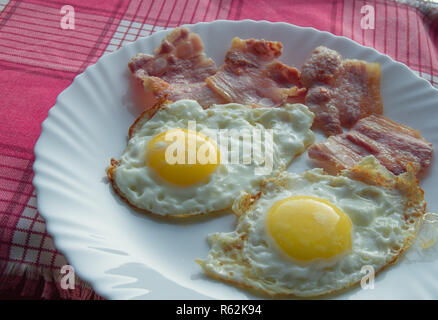 La deliziosa prima colazione - piastra bianca di uova fritte, pancetta su un tovagliolo rosso Foto Stock