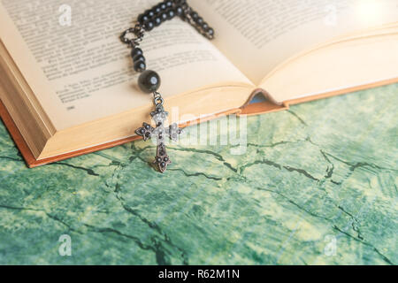 Rosario nero e la croce sulla Bibbia su una superficie verde. La religione a scuola. Foto Stock