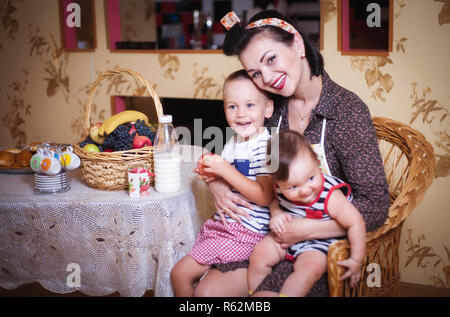 Ritratto di madre e due figli all'interno della cucina, girato in stile retrò. Studio shot, arredamento. Foto Stock