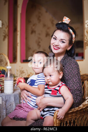 Ritratto di madre e due figli all'interno della cucina, girato in stile retrò. Studio shot, arredamento. Foto Stock