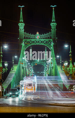 Budapest, Ungheria - addobbate a festa tram di luce (fenyvillamos) in movimento al ponte della Libertà (Szabadsag hid) di notte. Stagione di Natale a Budapest Foto Stock