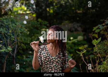 Una donna africana odorare una rosa in un giardino Foto Stock