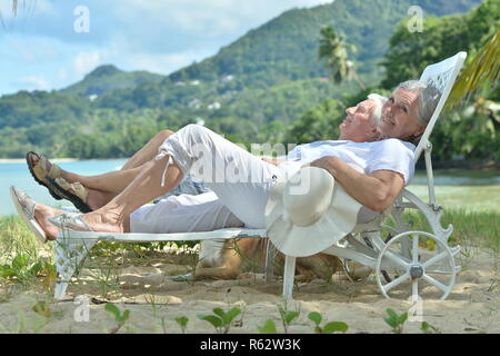 Ritratto di felice coppia di anziani in appoggio in chaise longue in spiaggia tropicale Foto Stock