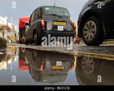 Westminster. Londra, Regno Unito. 3 dicembre, 2018. Una riflessione di Londra taxi nero nella pozza d'acqua di fronte Palazzo di Westminster. Pioggia pesante a Londra ha causato la raccolta di acqua. Credito: Dinendra Haria/Alamy Live News Foto Stock