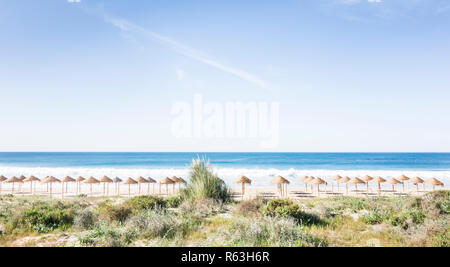 Di foglie di palma ombrelloni da spiaggia su una spiaggia deserta visto da una duna a alvor, algarve, portogallo Foto Stock