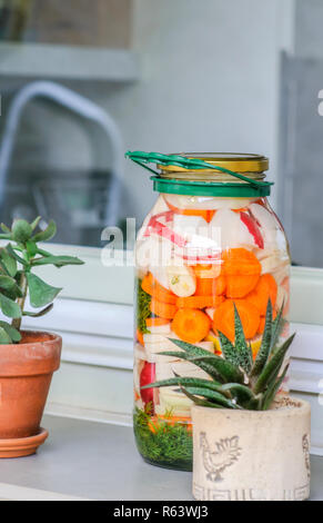 Vaso con varietà di fatti in casa verdure sottaceto esposta alla luce sul davanzale della cucina Foto Stock