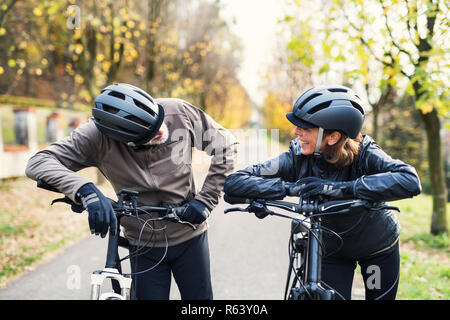 Attivo coppia senior con electrobikes in piedi all'aperto su una strada in natura. Foto Stock