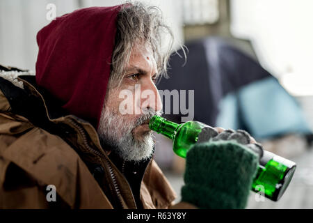 Una vista ravvicinata di senzatetto beggar man standing all aperto in città, bere. Foto Stock