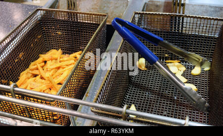 Due friggitrice cestelli affiancati. Uno con golden patatine fritte e gli altri con una cucina pinze. Foto Stock