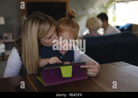 Madre baciando la sua figlia durante l'uso di digitale compressa in salotto Foto Stock