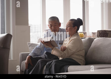 Coppia senior a discutere su una tavoletta digitale sul divano nel soggiorno Foto Stock