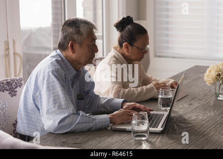 Coppia senior utilizzando laptop e tablet digitale sul tavolo da pranzo Foto Stock