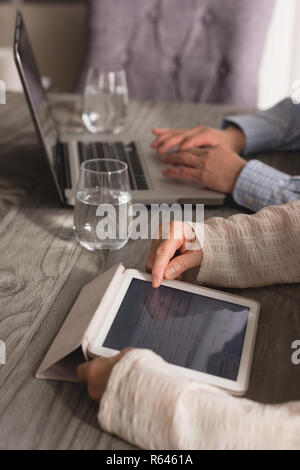 Coppia senior utilizzando laptop e tablet digitale sul tavolo da pranzo a casa Foto Stock